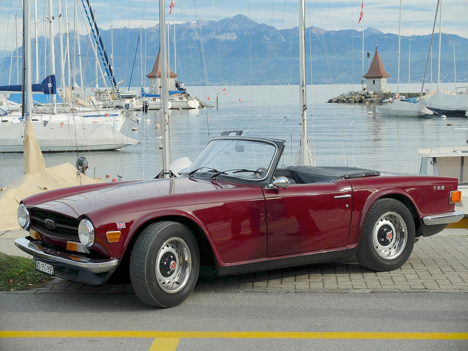 Dark red Triumph TR6 convertible parked by a harbour